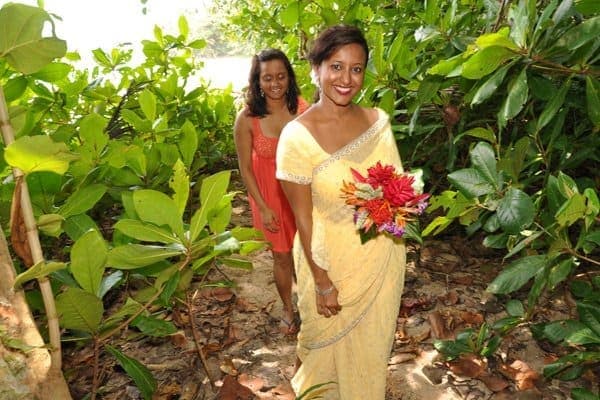 Bride walking the garden path to the beach, a bouquet of heliconias and tropical ginger in hand