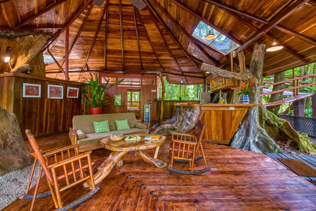 Upstairs living level — wooden rocking chairs around a low table, A-frame ceiling and the Sangrillo trunk passing through