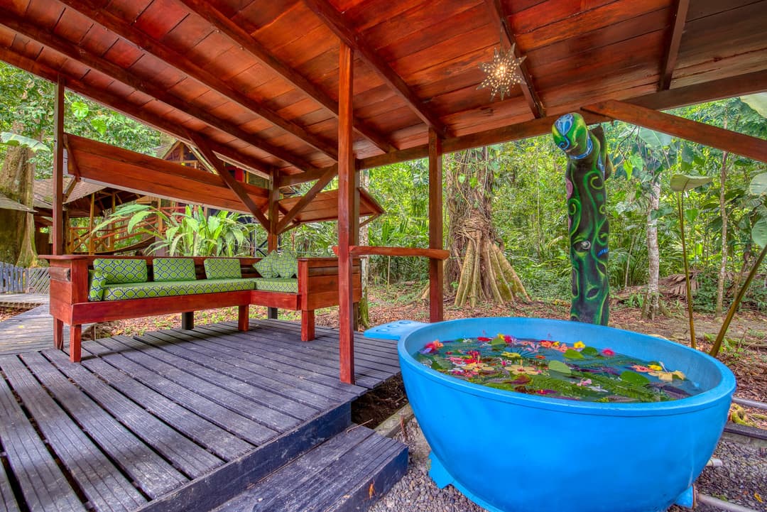Bright blue hot tub on the wooden deck beneath the rancho roof, daybed alongside, jungle behind